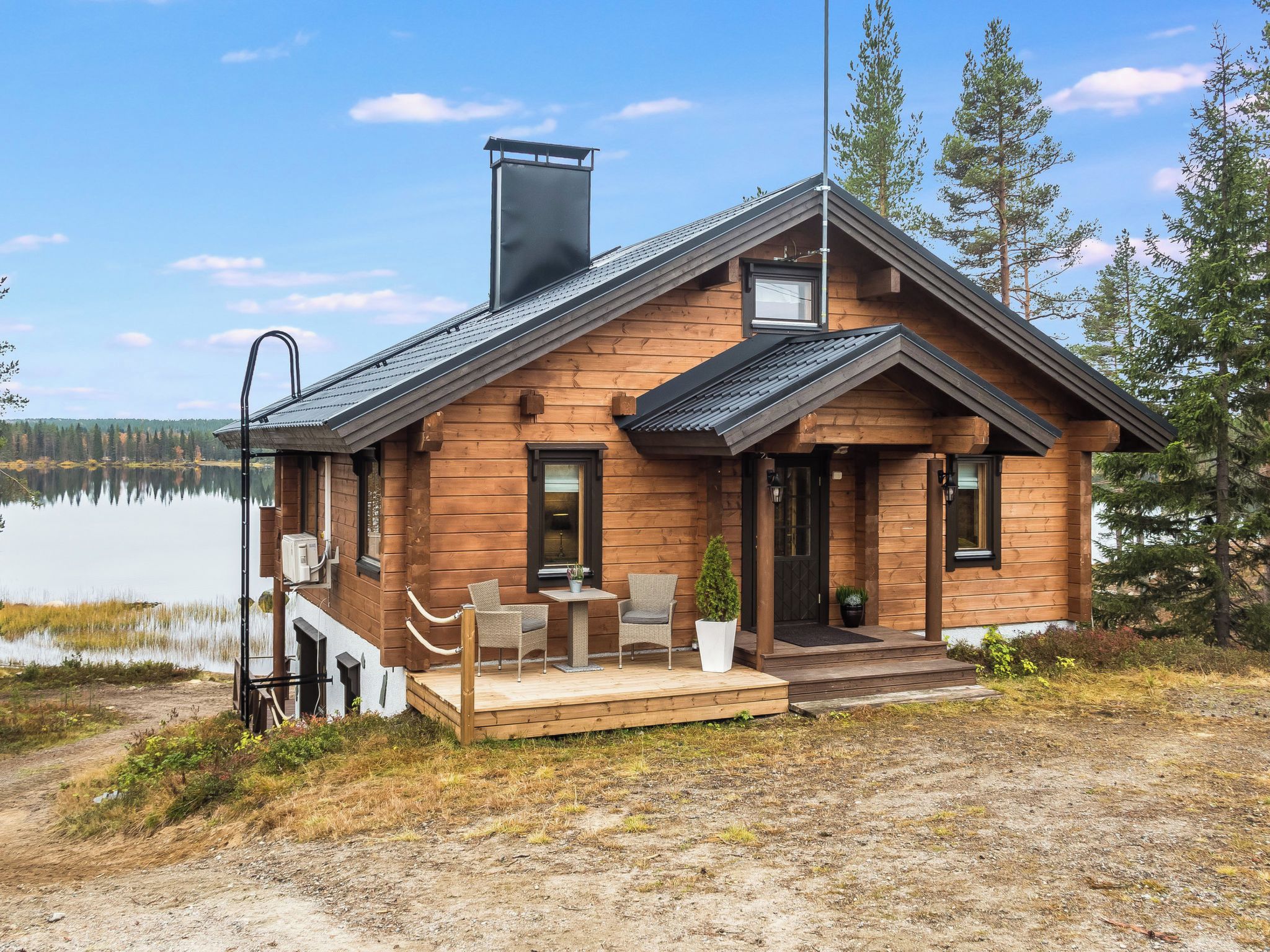 A wooden cabin with a deck, two chairs, and a small table.