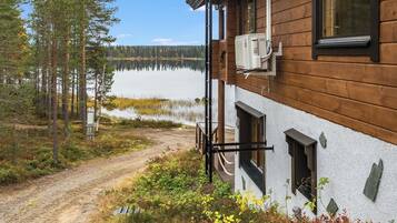 A cabin with a wooden exterior, a dirt path leading to it, and a lake in the background.