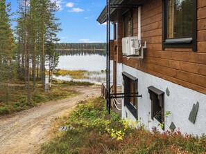 Una cabaña de madera con un sendero de tierra que conduce a ella, y un lago al fondo.