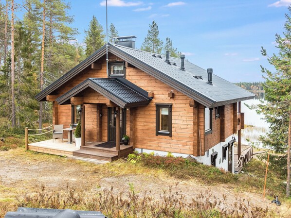 A wooden cabin with a sloped roof, a porch with seating, and a view of a lake.
