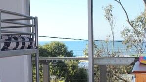 Ein Zimmer mit einem Etagenbett, einem Holzboden und einer großen Schiebetür, die auf einen Balkon mit Meerblick führt.