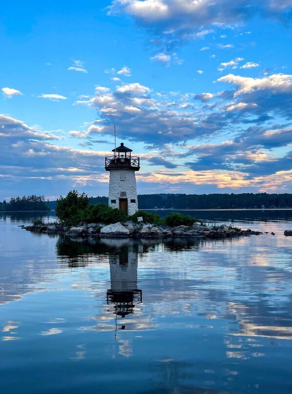 Un faro en una pequeña isla con aguas tranquilas que reflejan la estructura y el cielo.