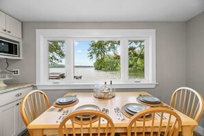 Un comedor con una mesa dispuesta para cuatro personas, microondas y vista a un lago desde una ventana.