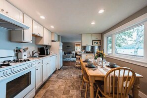 A kitchen with white cabinets, a stove, and a dining area with a table and chairs. - Cozy Keyes Cottage- Rare Lakefront Getaway (Winthrop)
