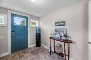 A hallway with a blue door, a water dispenser, a table with decorative items, and a sign that reads 'LAKE HOUSE'.