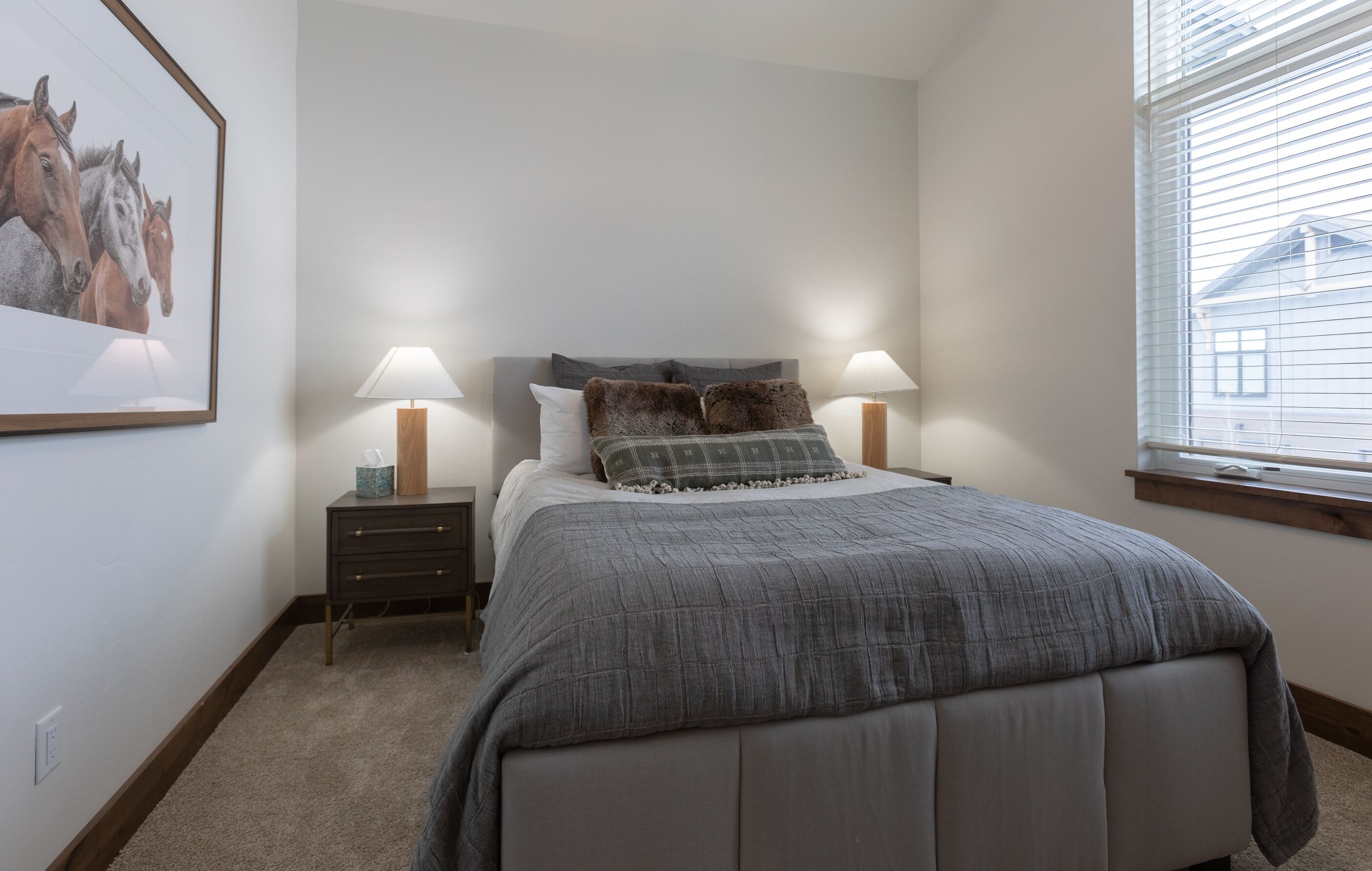Een slaapkamer met een groot bed, twee nachtkastjes met lampen, een ingelijst kunstwerk aan de muur en een raam met zonwering.