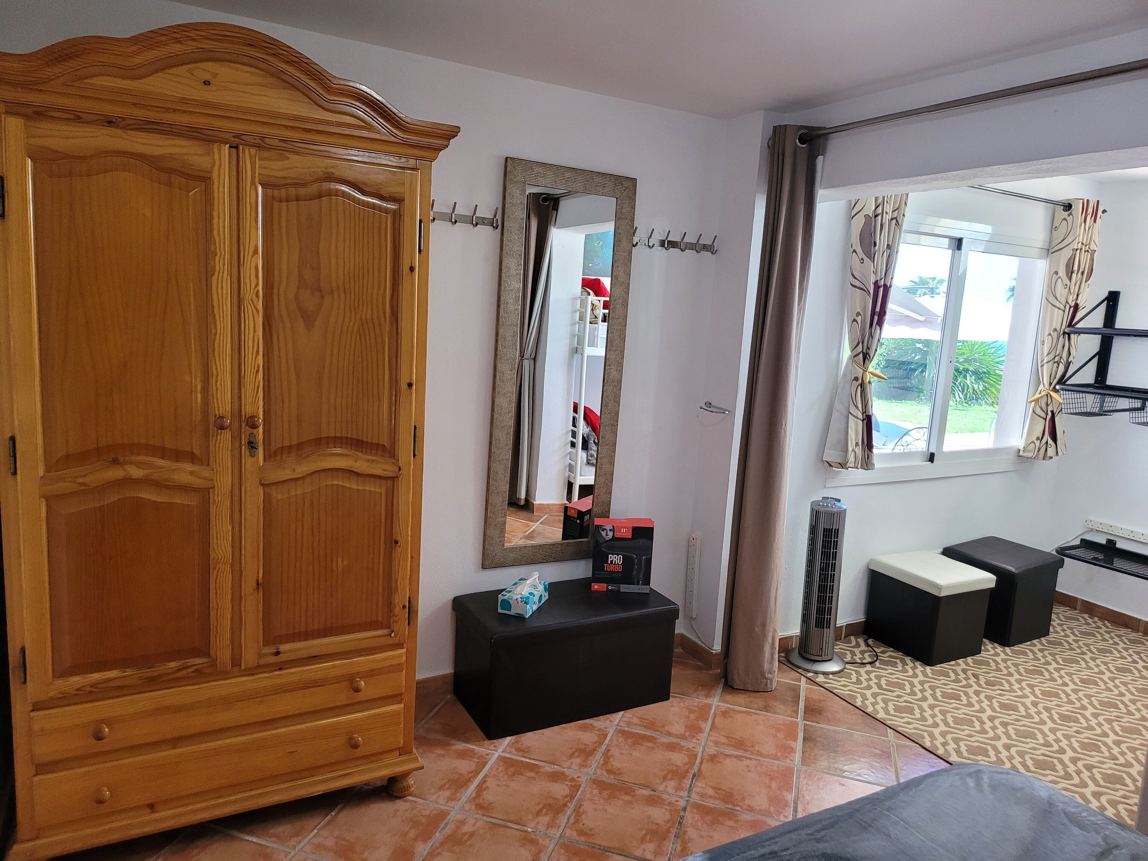 A room with a wooden wardrobe, a black table with a mirror, a window with curtains, and a radiator.