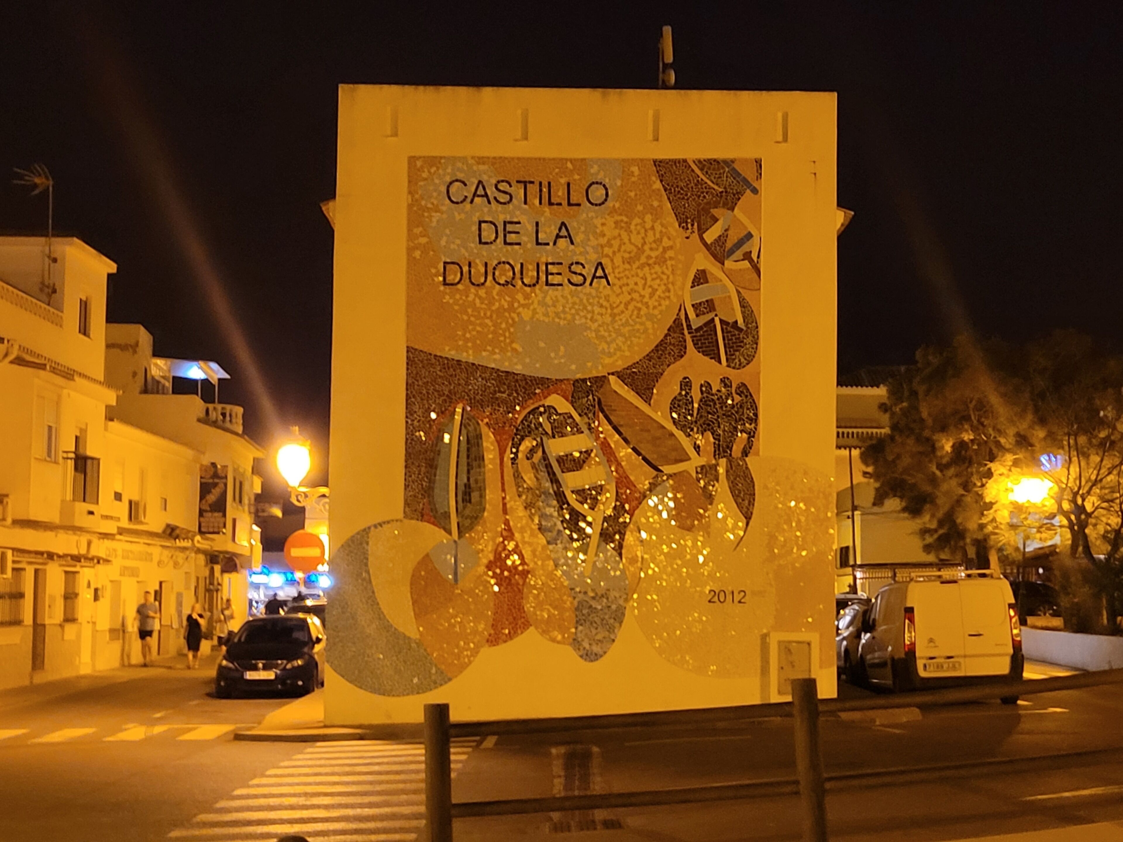 A nighttime street scene with a large billboard advertising "CASTILLO DE LA DUQUESSA" from 2012.