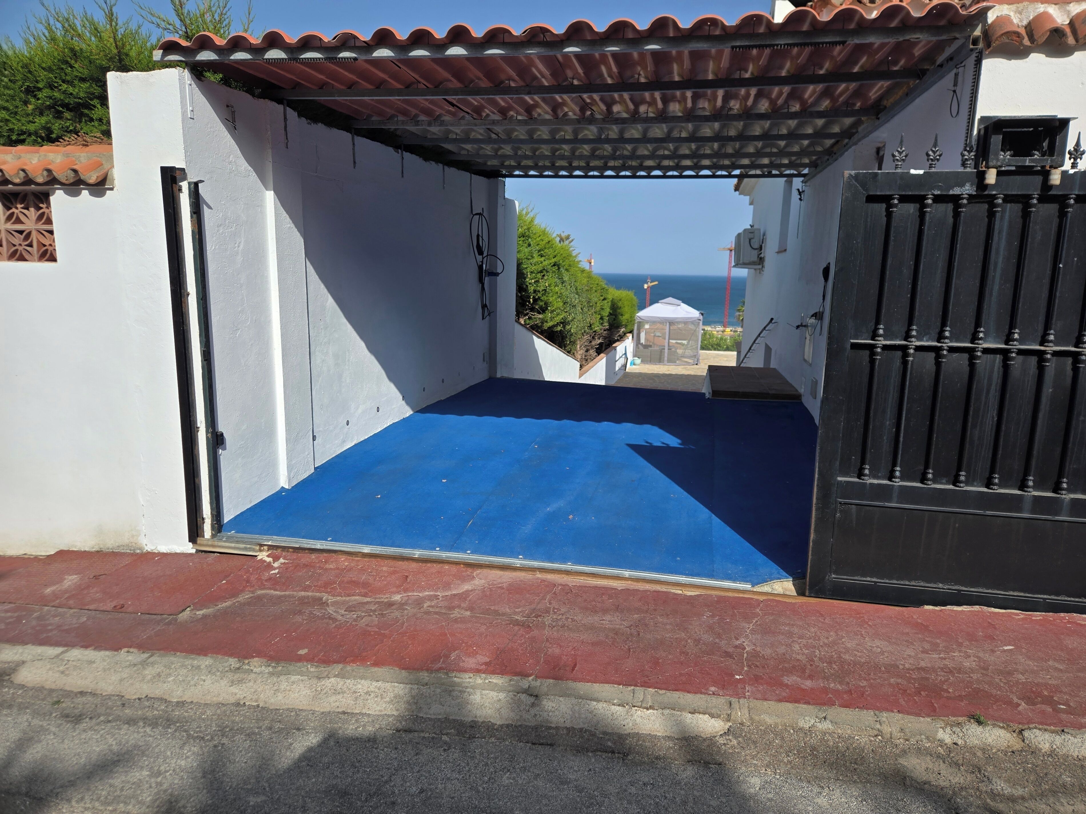 A covered outdoor area with a blue floor, a black gate, and a white wall.
