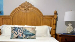 A neatly made bed with a wooden headboard, a decorative pillow, a bedside lamp, and a wall clock. - The Boat Shed (Christiansted)