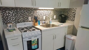 A kitchen with white cabinets, a stove, a sink, and a refrigerator. - The Boat Shed (Christiansted)