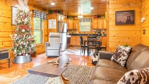 L’intérieur chaleureux d’un chalet en bois, avec un sapin de Noël, un coin repas et un salon comprenant un canapé et une table basse.