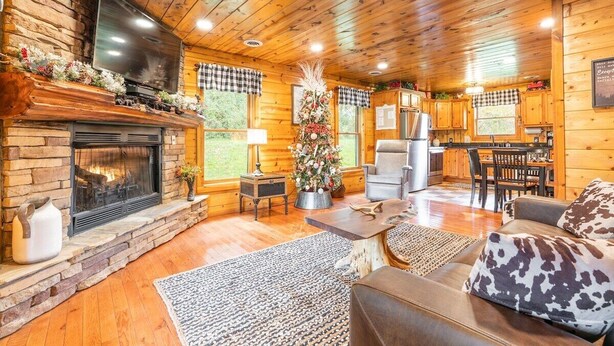 L’intérieur chaleureux d’un chalet avec une cheminée en pierre, des murs en bois, un coin repas et un salon doté d’un canapé en cuir.
