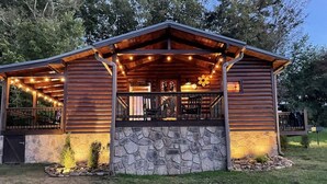 Une cabane en bois avec des fondations en pierre, une véranda couverte et des guirlandes lumineuses.