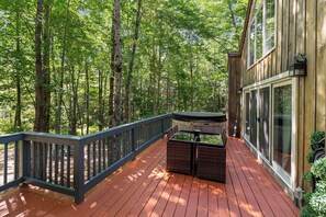 A wooden deck with a hot tub, surrounded by trees.