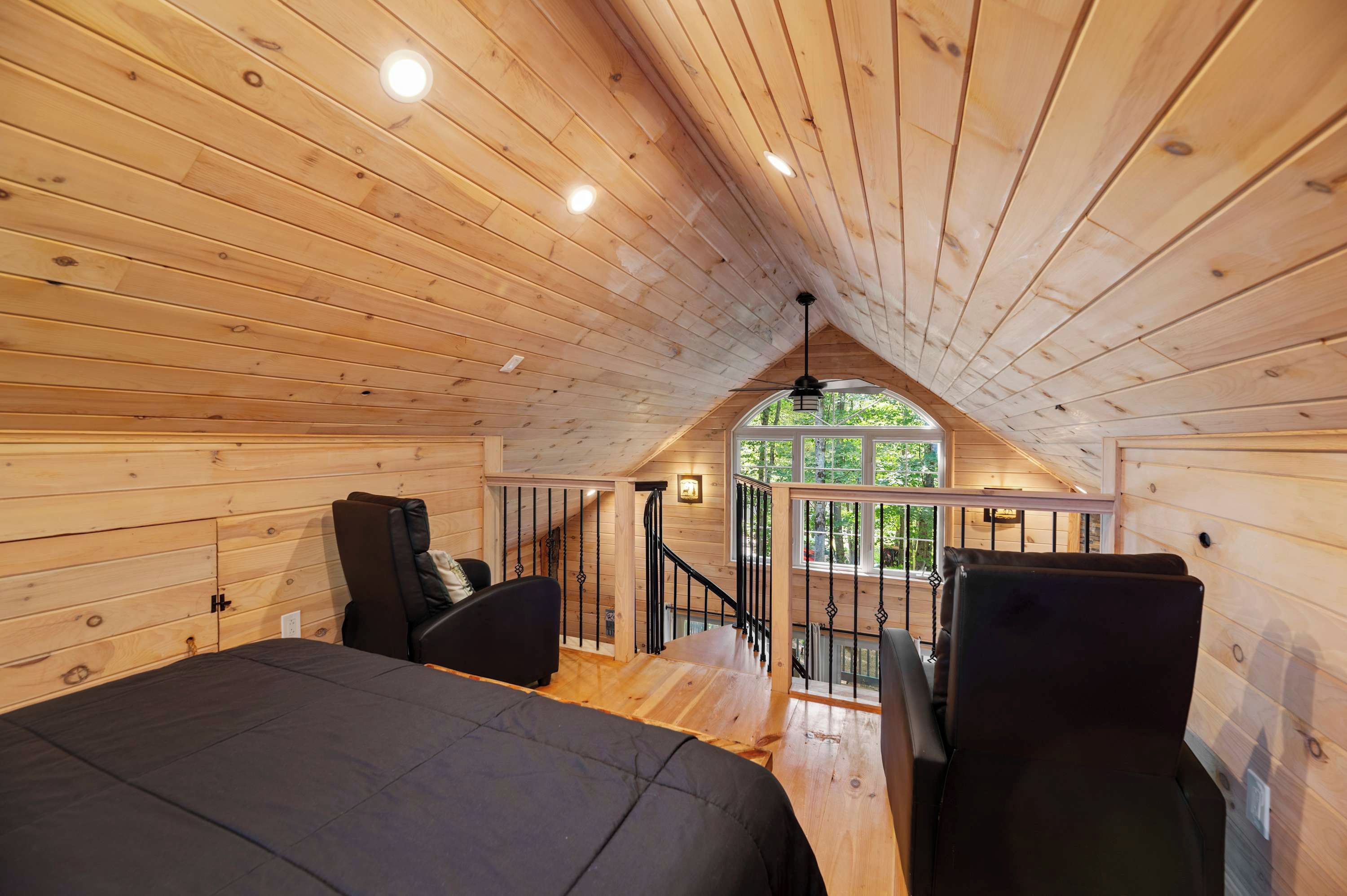 Een houten chaletinterieur met een slaapkamer op een entresol, een trap en uitzicht op het omliggende landschap.