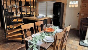 Een houten interieur met een eettafel voor vier personen, omringd door houten stoelen. Een spiltrap met zwarte metalen leuningen is op de achtergrond zichtbaar.