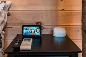 Uno smartphone su un tavolo mostra un film, con un telecomando e un dispositivo bianco, forse una cassa audio o una base di ricarica.