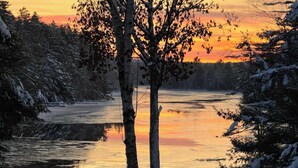 Une rivière gelée, bordée d’arbres des deux côtés, qui reflète le coucher de soleil.