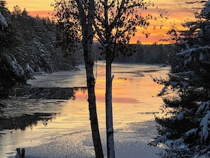 Un fiume ghiacciato con alberi su entrambe le rive, che riflette il tramonto.