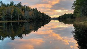 Une rivière paisible où se reflètent les arbres et le ciel au coucher du soleil.