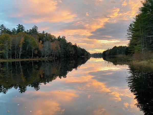 A calm river reflecting trees and a sunset sky.