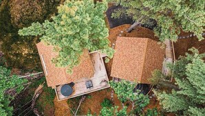 Twee houten hutten met aanleunterrassen, omgeven door dicht bos.