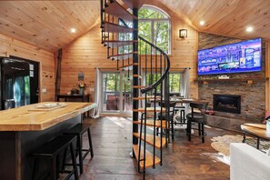 A wooden interior with a spiral staircase, a kitchen area, a dining space, and a fireplace. - MoonLight Treehouse | Hot Tub · Lakefront Retreat (Belgrade)