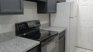 Una cocina con armarios oscuros, una estufa negra, un refrigerador blanco y encimeras de granito.