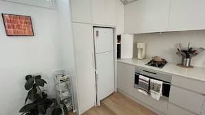 A modern kitchen with white cabinets, a built-in oven, a coffee machine, and a plant. - Spacious Manly Studio (Fairlight)