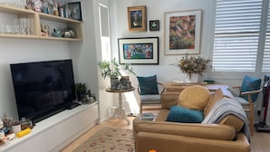 A living room with a sofa, TV, and decorative items. - Spacious Manly Studio (Fairlight)