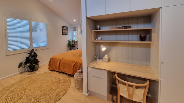 A bedroom with a bed, bedside table, lamp, and a desk area with shelves. - Spacious Manly Studio (Fairlight)