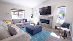 Ein modernes Wohnzimmer mit einer Couch, einem Hocker und einem flachbildfernseher an der Wand.