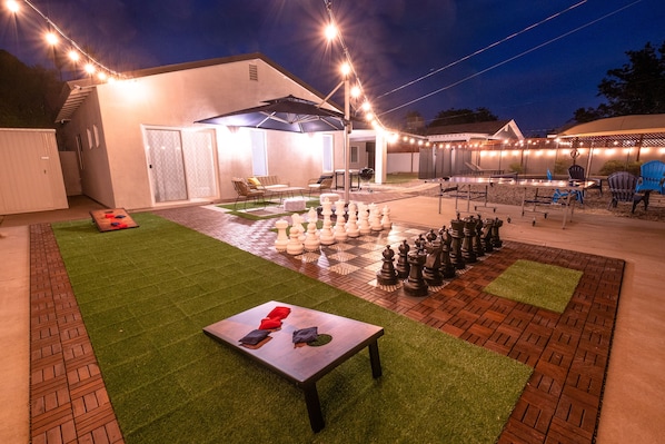 An outdoor patio area with a chessboard, a table with chairs, and string lights.