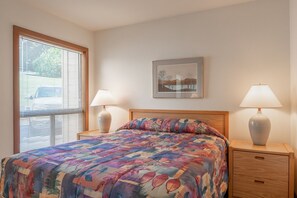 Une chambre à coucher avec un lit, deux tables de chevet, une fenêtre avec des stores et un tableau encadré au mur.