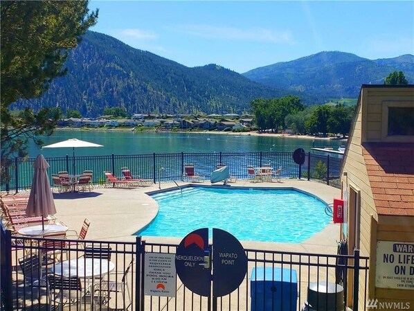 Une piscine entourée d’une clôture, avec des chaises longues et des parasols.