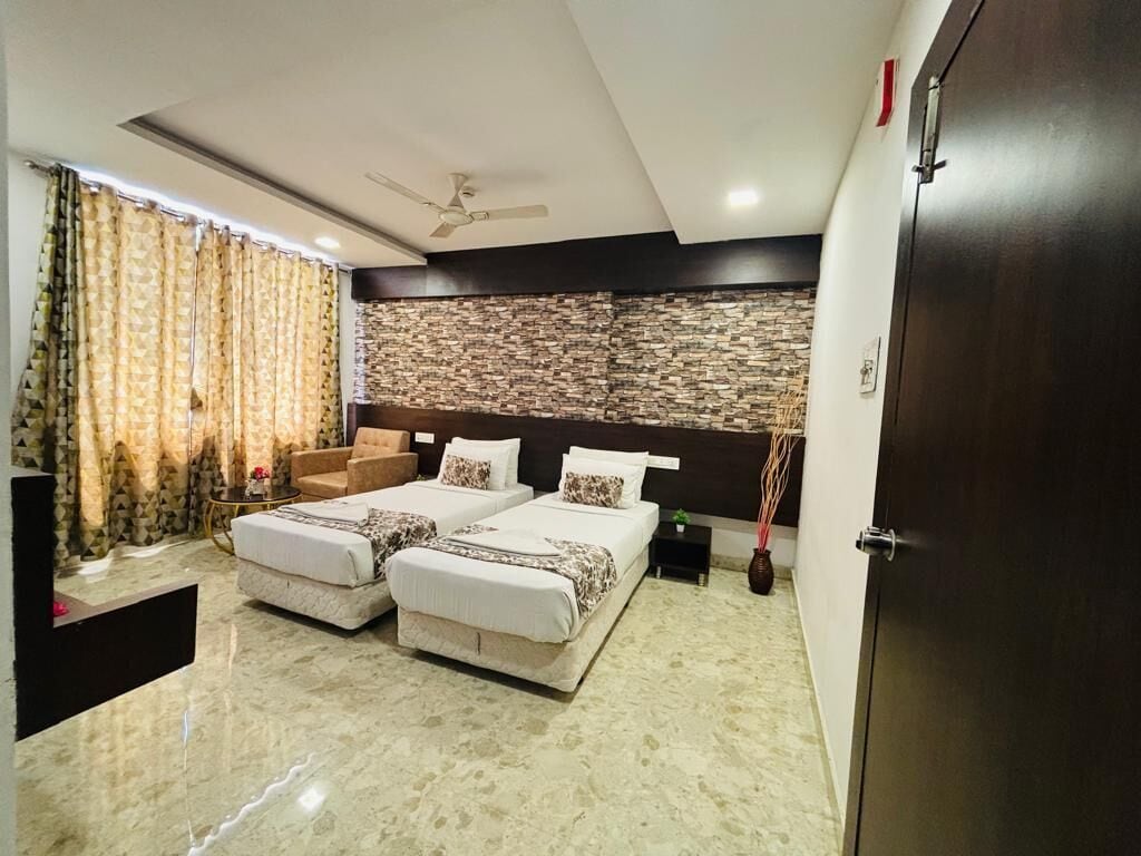 A modern bedroom with two beds, a ceiling fan, a stone-patterned wall, and a dark wooden door.