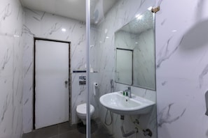 A bathroom with a white marble wall, a glass shower enclosure, a white sink, and a toilet. - Hotel Signature Airport zone hyderabad (Hyderabad)