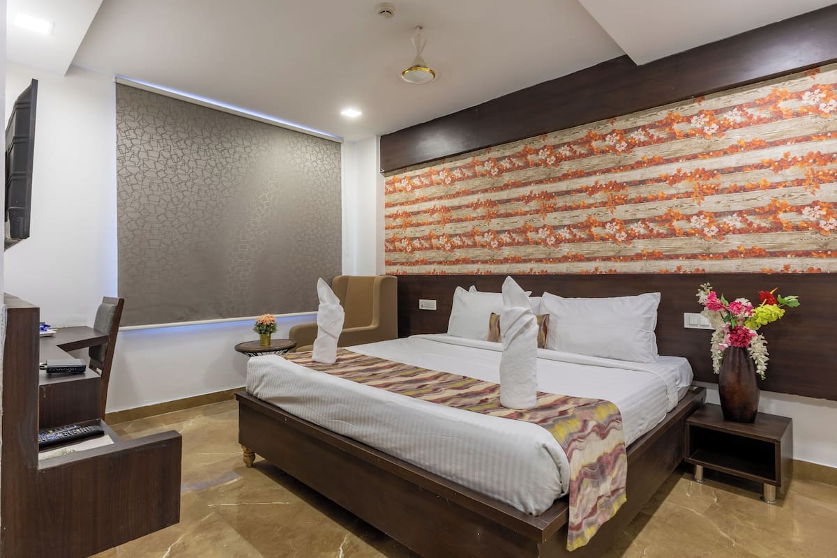 Ein modernes Hotelzimmer mit einem großen Bett, einem Schreibtisch mit Stuhl, einem kleinen Tisch und einer Blumenvase.