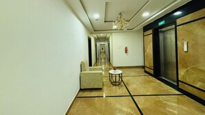 A hotel corridor with a marble floor, a sofa, a small round table, an elevator, and a chandelier. - Hotel Signature Airport zone hyderabad (Hyderabad)