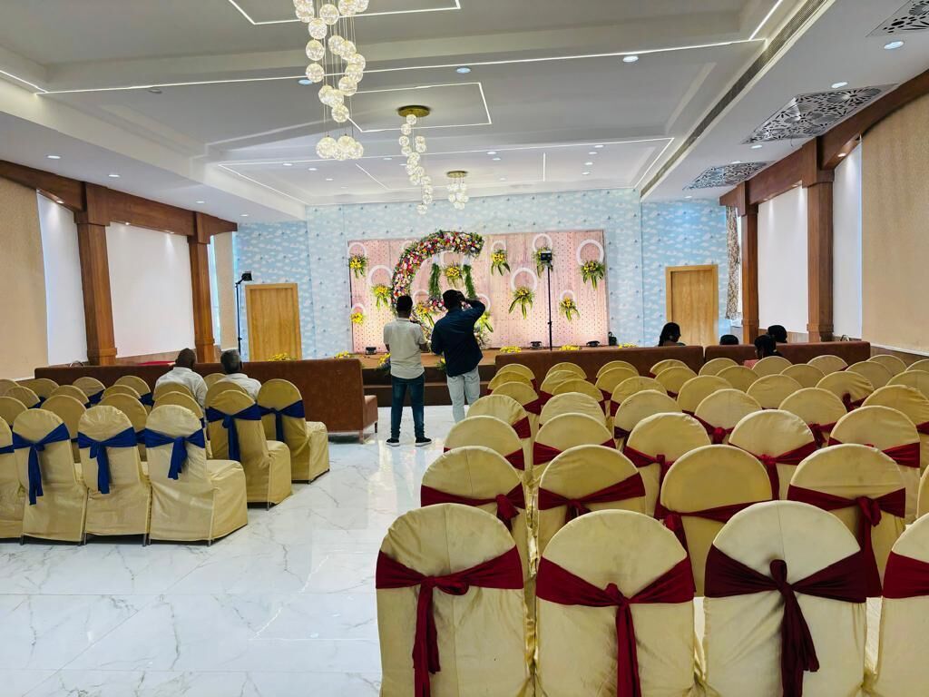 Une salle de conférence avec des rangées de chaises, une scène décorée de fleurs et un pupitre.