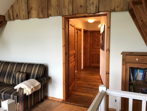 A cozy room with a plaid sofa, a wooden bookshelf, and a wooden staircase leading to another room.