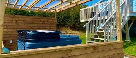 A wooden pergola structure with a hot tub and a staircase leading to a higher level.