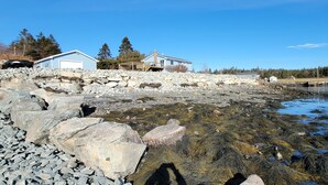 A coastal property with a stone wall, a wooden deck, and a clear view of the sea. - Tangier Oceanfront Escape with Hot Tub, Sauna & Kayaks (Tangier)