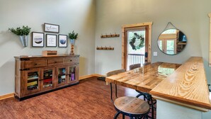 Un comedor con una mesa y sillas de madera, un armario de madera con puertas de cristal y obras de arte colgadas en la pared.