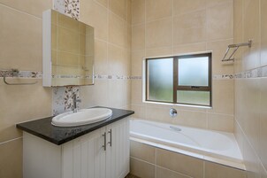 A bathroom with a white sink, a mirror, a window, and a bathtub.