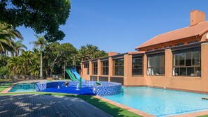 A swimming pool with a slide, surrounded by palm trees and a building with large windows. - San Lameer Villa Rentals 14321 (Southbroom)