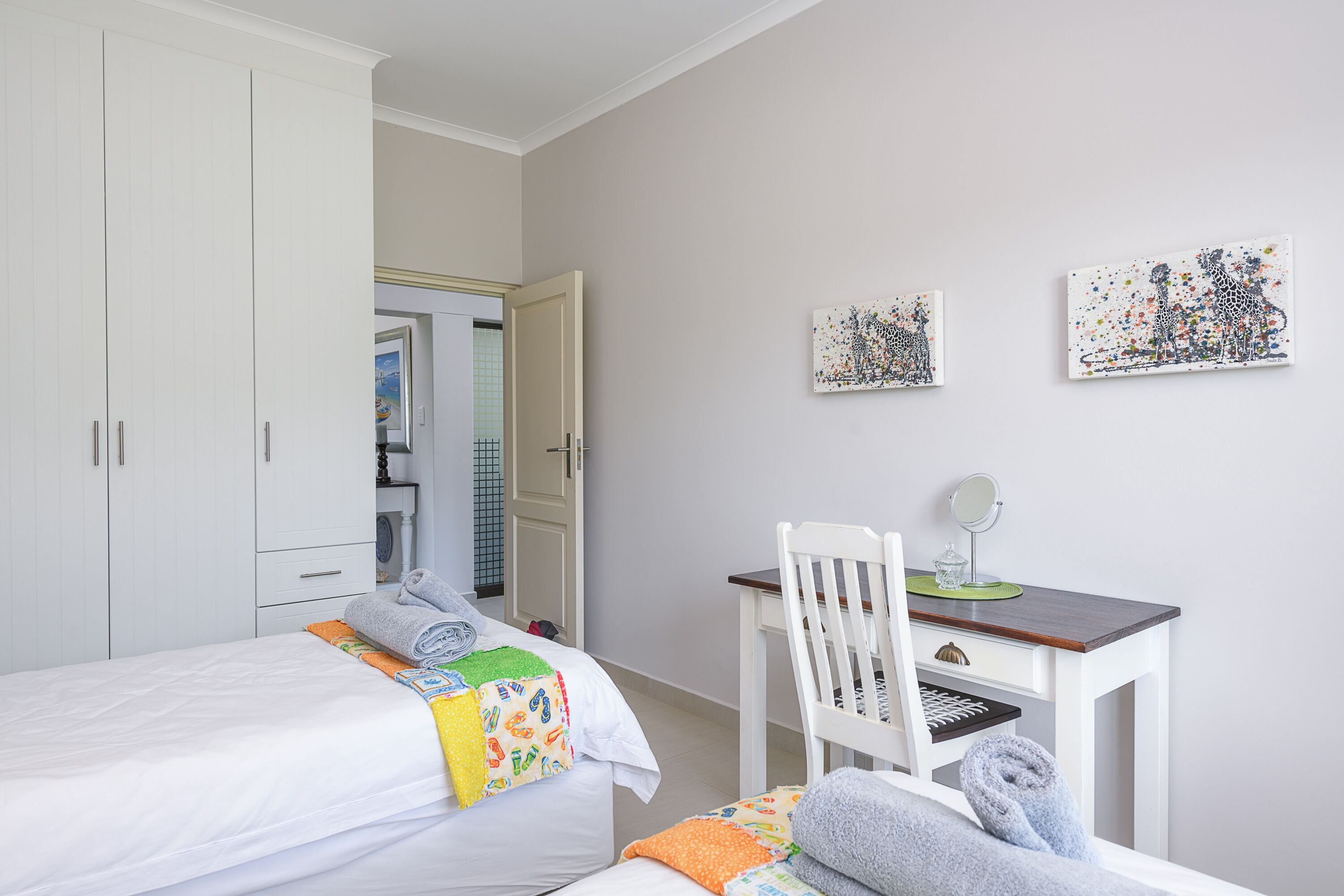 Um quarto com uma cama, uma escrivaninha, uma cadeira e duas obras de arte na parede.