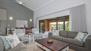 A spacious living room with a grey sofa, a wooden coffee table, and a dining area with a white table and chairs. - San Lameer Villa Rentals 14321 (Southbroom)