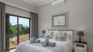 A bedroom with a large bed, two bedside tables with lamps, a framed artwork on the wall, and a view of greenery through the window. - San Lameer Villa Rentals 14321 (Southbroom)